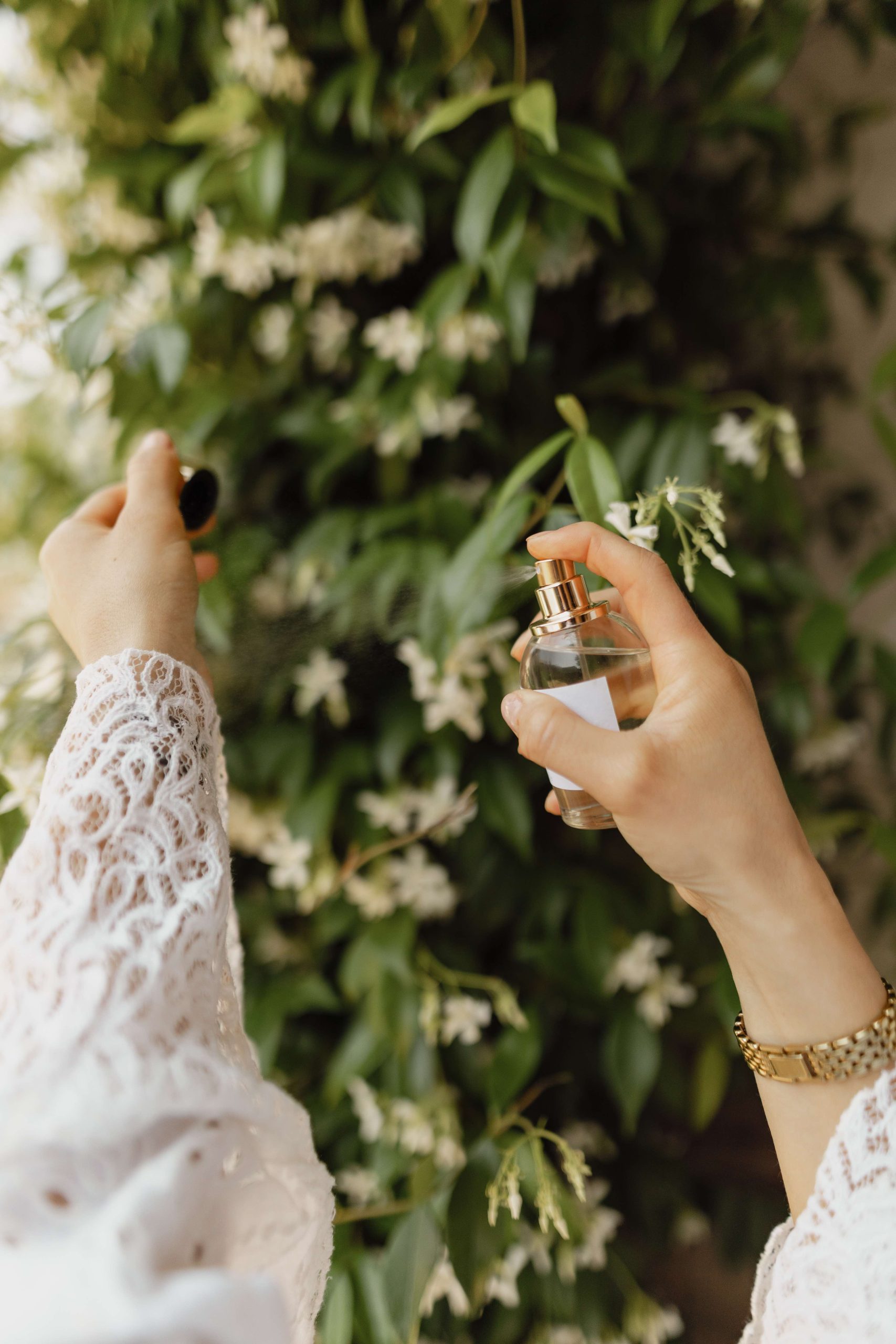 Mani che aprono una boccetta di profumo artigianale Atelier Nativa spruzzata su una parete di gelsomino rampicante per la guida alla scelta del profumo da donna